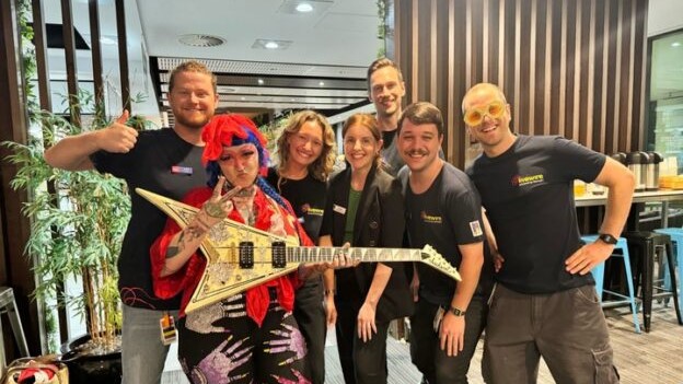 The LW RCH team! There are four men and three women. One of the women is holding a guitar and has very colourful hair and clothes. The rest of the team are in LW uniforms. They are standing in a big room with a plant behind them.